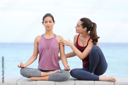 Yogi teaching yoga pose to student on the beach