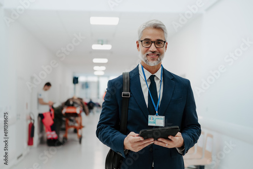 Portrait of pharmaceutical sales representative in medical building, waiting for doctor, presenting new pharmaceutical product. Smiling drug rep standing in hall holding tablet.