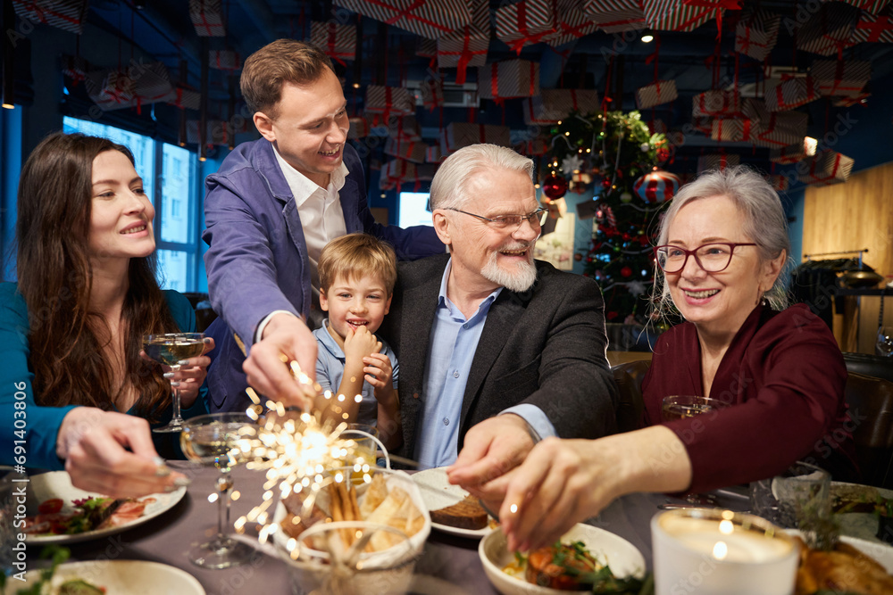 Joyful family celebrating New Year in restaurant with sparkling