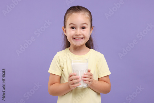 Cute girl with glass of fresh milk on violet background