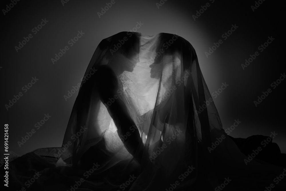 black and white photo of sensual multiracial couple covered with bedsheet sitting on floor together