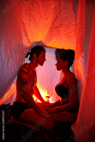 sexy diverse couple sitting under bedsheet and posing alluringly surrounded by lights, together photo