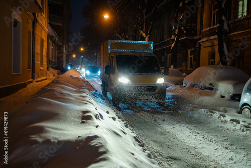 Yellow lorry van moving at night in the heavy snowfall on a snowy street with lights on photo