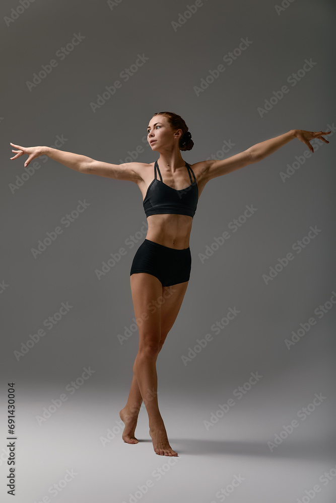 Side view of a dancing pretty ballerina wearing a black criss-cross back leotard isolated over a gray background