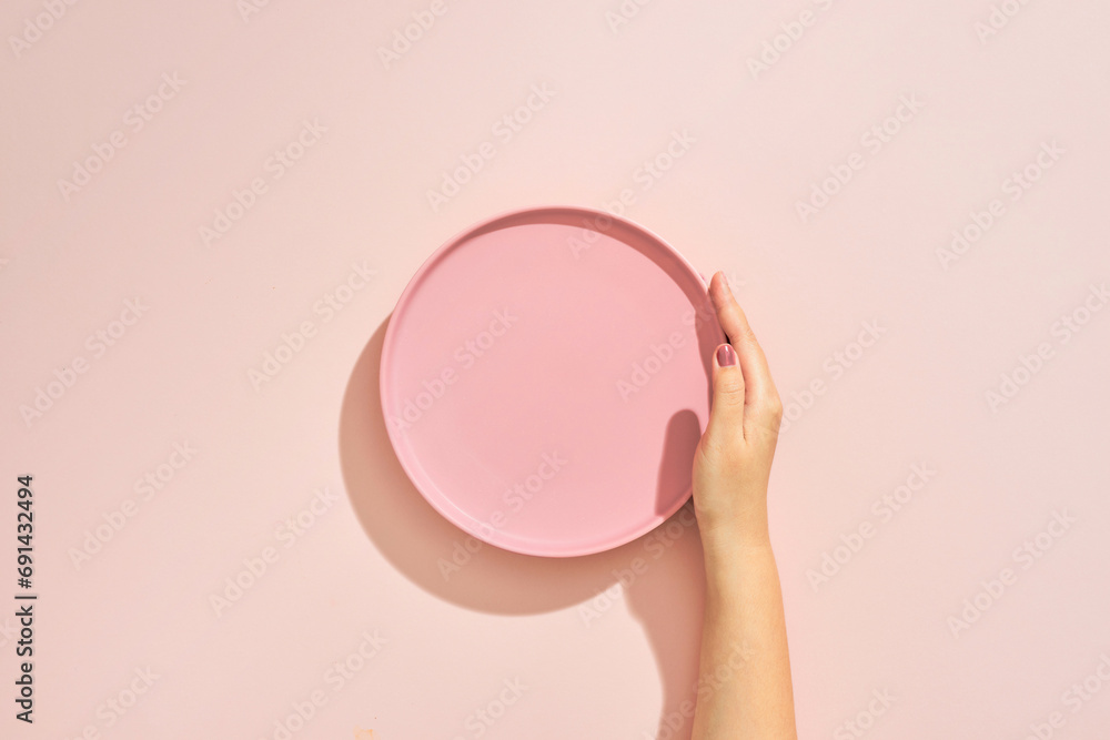 A female hands hold a empty(blank) pink dish(plate) on pink table(desk)