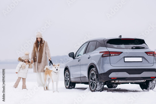 Woman with her daughter and dog having a walk in a snowy park by their car