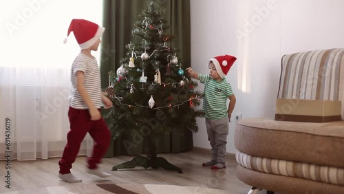 Two little boys, two brothers decorate the Christmas tree at home. Little boys in Christmas caps. A family with children is preparing for the New Year