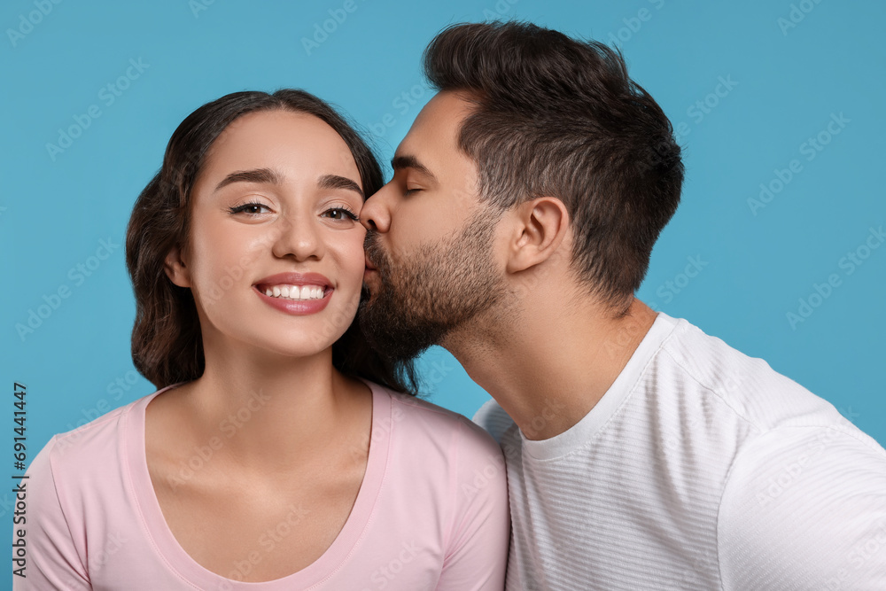 Man kissing his smiling girlfriend on light blue background Man kissing his smiling girlfriend on light blue background