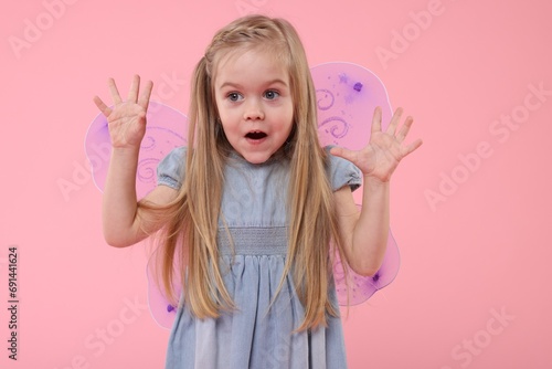 Cute little girl in fairy costume with violet wings on pink background