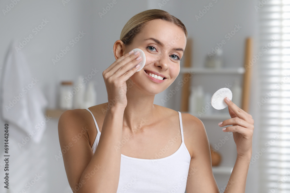 Smiling woman removing makeup with cotton pads in bathroom Smiling woman removing makeup with cotton pads in bathroom