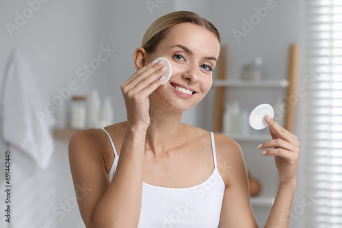 Smiling woman removing makeup with cotton pads in bathroom