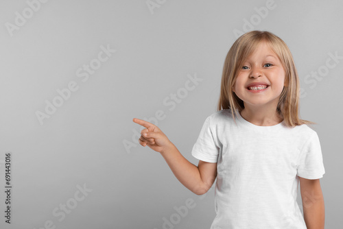 Special promotion. Smiling girl pointing at something on grey background. Space for text photo