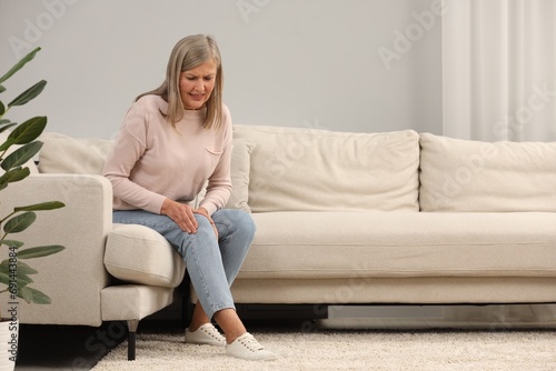 Mature woman suffering from knee pain on sofa at home. Rheumatism symptom photo