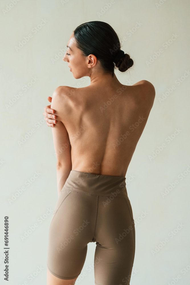 Back view, showing the spine, without bra. Young woman with slim body type is in fitness clothes in the studio Back view, showing the spine, without bra. Young woman with slim body type is in fitness clothes in the studio