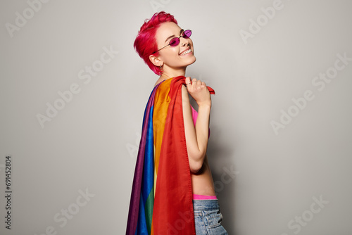 young and pleased female activist with pink hair and sunglasses posing with lgbt rainbow flag