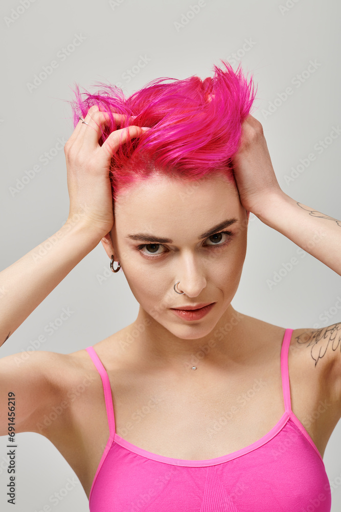 Naklejka premium portrait of alluring young woman with pink hair and tattoos posing and touching her hair, fashion
