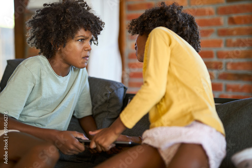 Small black kids  fighting over digital tablet on sofa at home photo