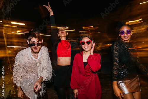 Joyful group of diverse friends partying outdoors at night, showcasing fashion and fun.