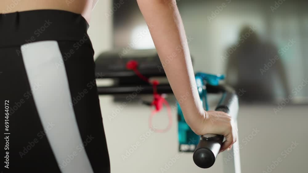 Woman leans on treadmill handle resting in gym closeup. Sportswoman taps on bar standing on trainer machine in sports club slow motion. Fitness activity Woman leans on treadmill handle resting in gym closeup. Sportswoman taps on bar standing on trainer machine in sports club slow motion. Fitness activity