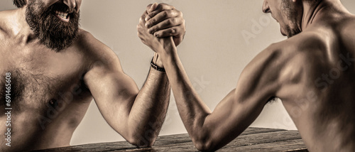 Arms wrestling thin hand, big strong arm in studio. Two man's hands clasped arm wrestling, strong and weak, unequal match. Heavily muscled bearded man arm wrestling a puny weak man photo