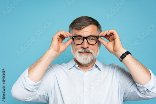 Happy caucasian mature man trying new glasses and smiling, standing on blue background
