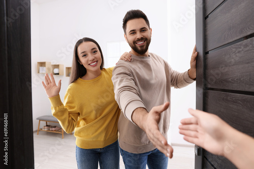 Happy couple welcoming their guest near door. Invitation to come indoors photo