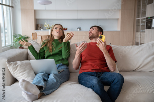 Fotografija Displeased couple sitting on sofa, having emotional stress, discomfort, headache, feeling nervous from loud resentful noise, sound, knock from neighboring flat