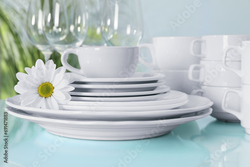 Set of clean dishware and flower on light blue table, closeup
