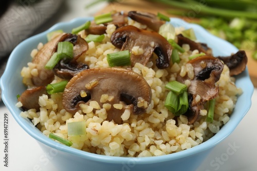 Delicious bulgur with mushrooms and green onion in bowl on table, closeup