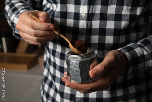 Man putting ground coffee into moka pot indoors, closeup photo