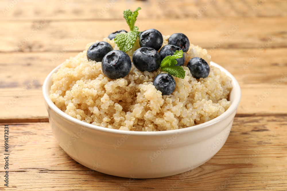 Tasty quinoa porridge with blueberries and mint in bowl on wooden table, closeup Tasty quinoa porridge with blueberries and mint in bowl on wooden table, closeup