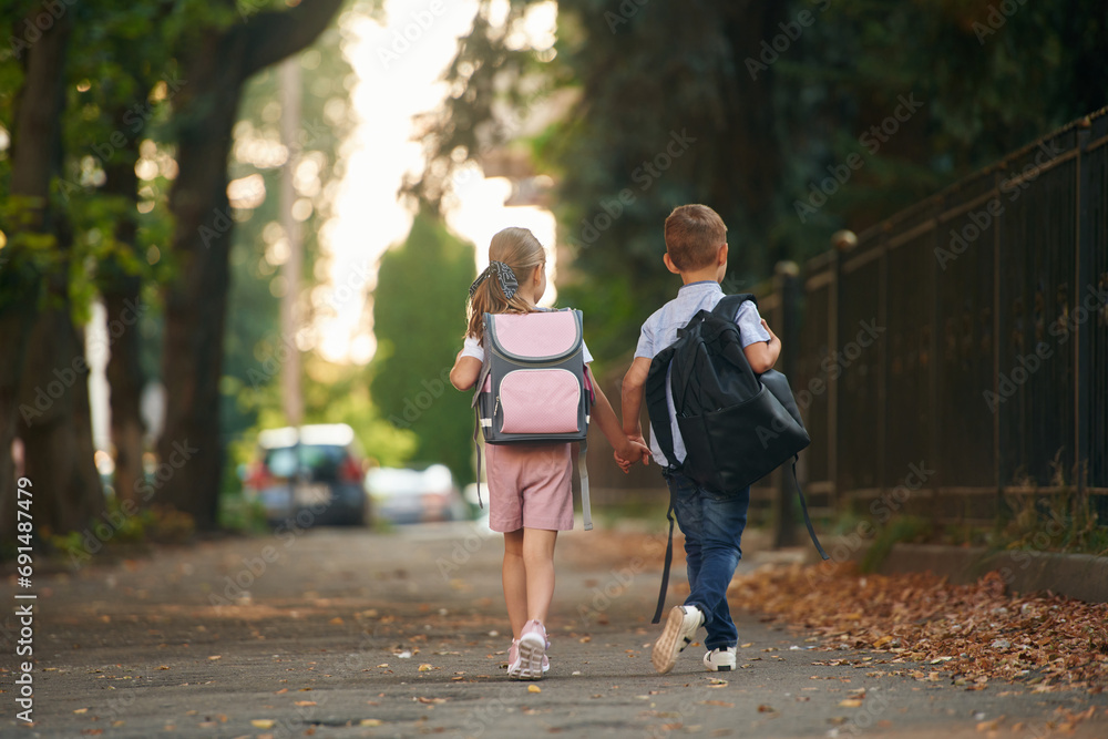 Back view, walking. Young school children of boy and girl are together outdoors Back view, walking. Young school children of boy and girl are together outdoors