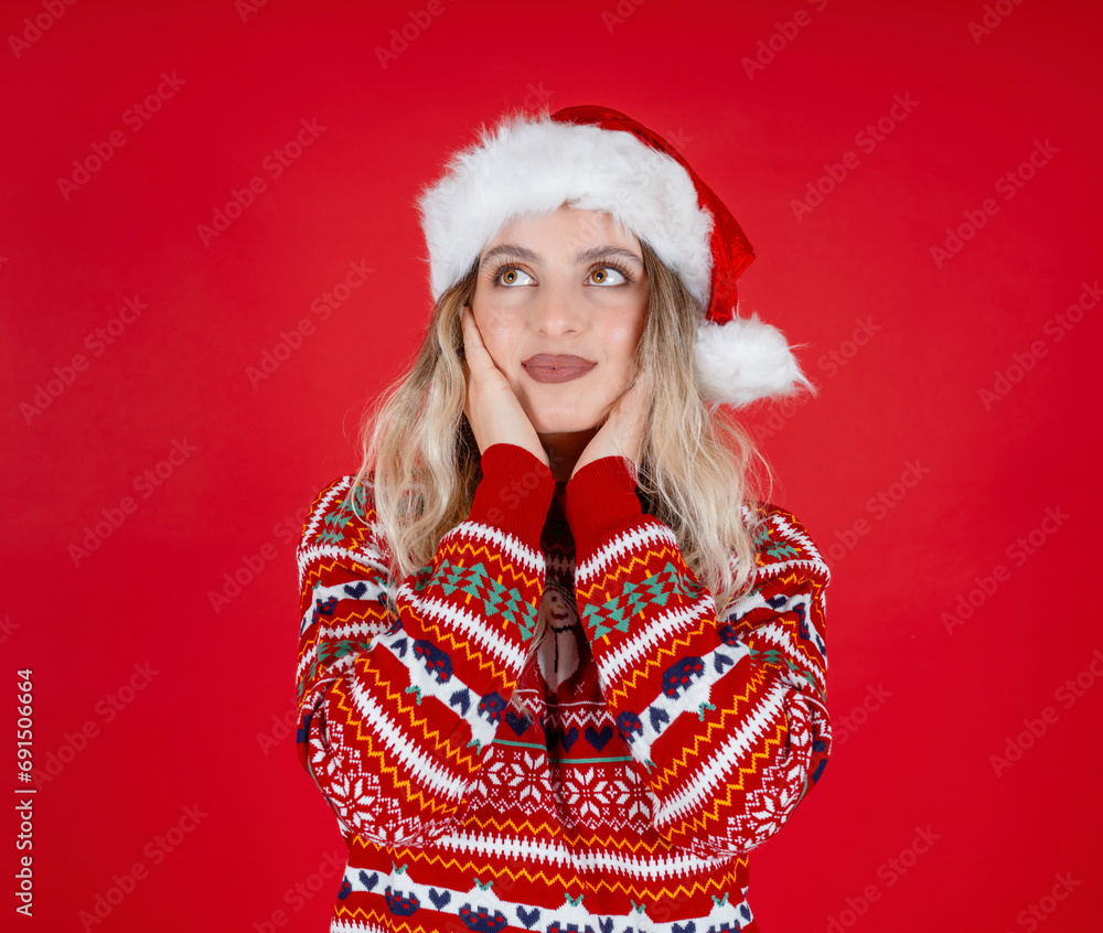 Pretty cute positive Santa woman, portrait of young caucasian blonde pretty cute positive Santa woman. Wear festive hat, cozy warm knitted sweater. Hold face hands. Red background. Copy space. Pretty cute positive Santa woman, portrait of young caucasian blonde pretty cute positive Santa woman. Wear festive hat, cozy warm knitted sweater. Hold face hands. Red background. Copy space.
