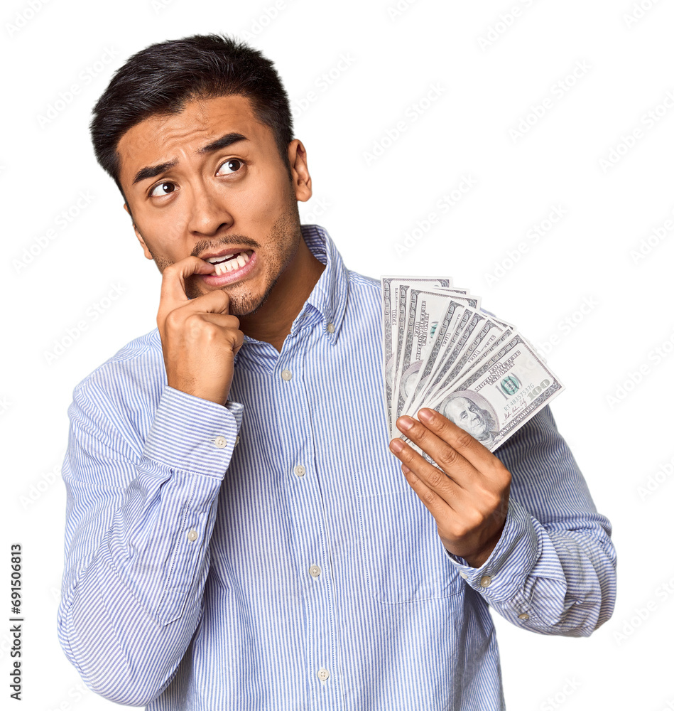 Young Chinese man holding dollar bills in studio relaxed thinking about something looking at a copy space. Young Chinese man holding dollar bills in studio relaxed thinking about something looking at a copy space.