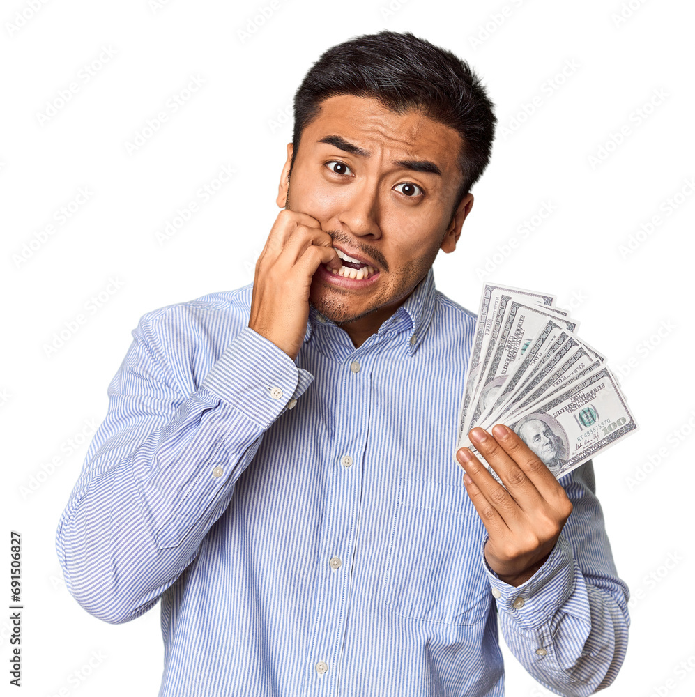 Young Chinese man holding dollar bills in studio biting fingernails, nervous and very anxious. Young Chinese man holding dollar bills in studio biting fingernails, nervous and very anxious.