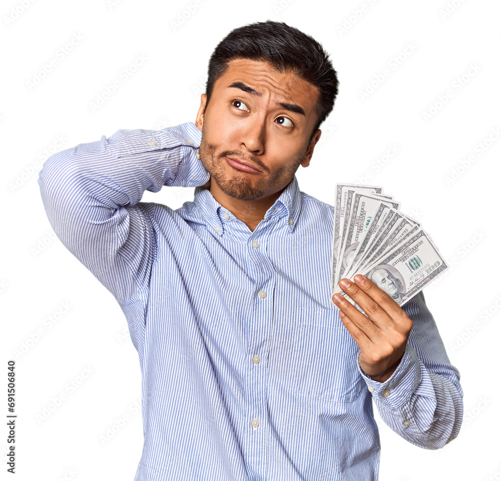 Young Chinese man holding dollar bills in studio touching back of head, thinking and making a choice. Young Chinese man holding dollar bills in studio touching back of head, thinking and making a choice.