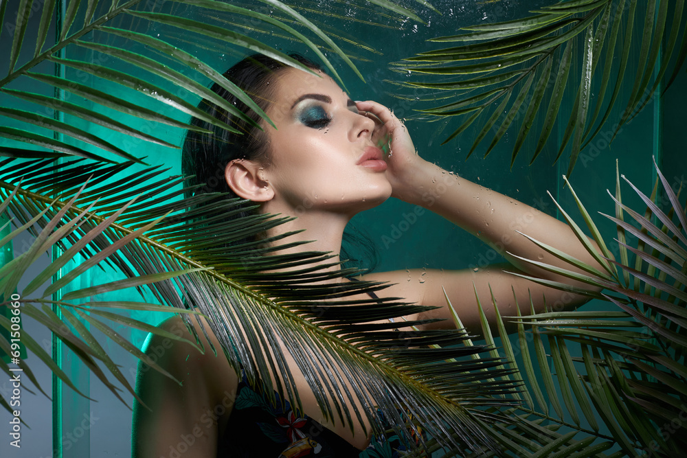 Beauty tropical portrait of a woman in palm leaves, wet long hair, green eye shadow makeup Beauty tropical portrait of a woman in palm leaves, wet long hair, green eye shadow makeup
