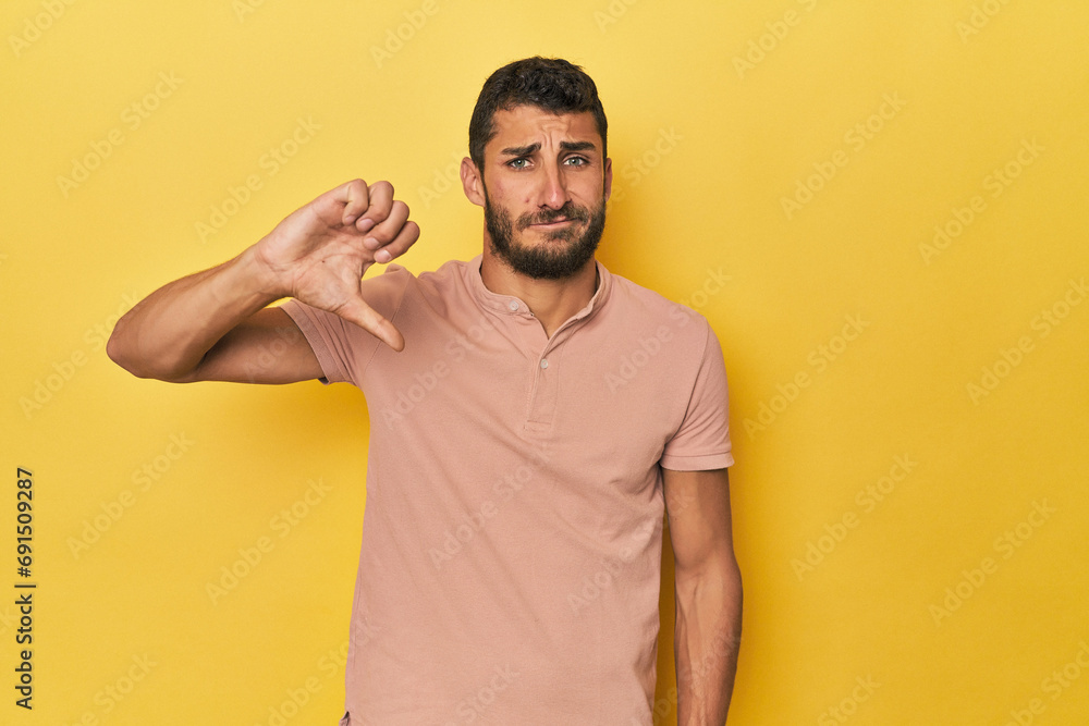 Young Hispanic man on yellow background showing a dislike gesture, thumbs down. Disagreement concept. Young Hispanic man on yellow background showing a dislike gesture, thumbs down. Disagreement concept.