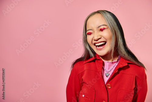 Valentines day concept, happy asian woman with heart eye makeup laughing on pink background photo