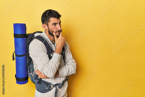 Young Hispanic man ready for hiking looking sideways with doubtful and skeptical expression. © Asier
