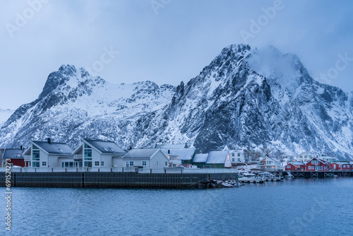 Winter scenic view of a Lofoten village with white and red typical houses and snowcapped mountains in the background