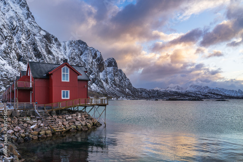 Typical Lofoten red rorbuer house with wooden pier at sunset with snowcapped mountains