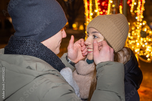 Positive, cheerful couple hugging during x-mas evening. Decorated lights on the streets outdoors (ID: 691532622)