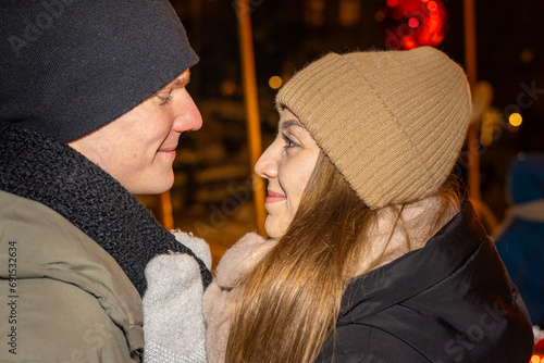 Positive, cheerful couple hugging during x-mas evening. Decorated lights on the streets outdoors (ID: 691532634)