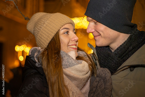 Positive, cheerful couple hugging during x-mas evening. Decorated lights on the streets outdoors (ID: 691532637)