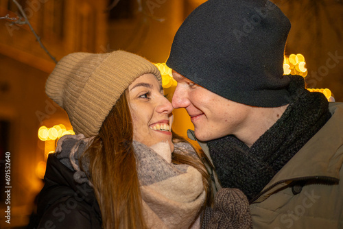Positive, cheerful couple hugging during x-mas evening. Decorated lights on the streets outdoors (ID: 691532640)