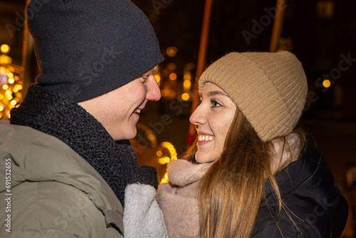 Positive, cheerful couple hugging during x-mas evening. Decorated lights on the streets outdoors (ID: 691532655)