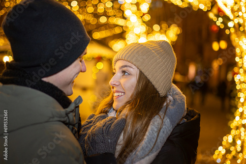 Positive, cheerful couple hugging during x-mas evening. Decorated lights on the streets outdoors (ID: 691532661)