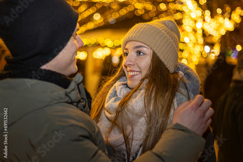 Positive, cheerful couple hugging during x-mas evening. Decorated lights on the streets outdoors (ID: 691532662)