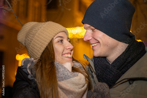 Positive, cheerful couple hugging during x-mas evening. Decorated lights on the streets outdoors (ID: 691532665)